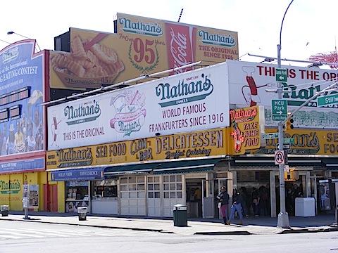 This yellow and white building is covered with signs
            proclaiming Nathan's World Famous Frankfurters since 1916.