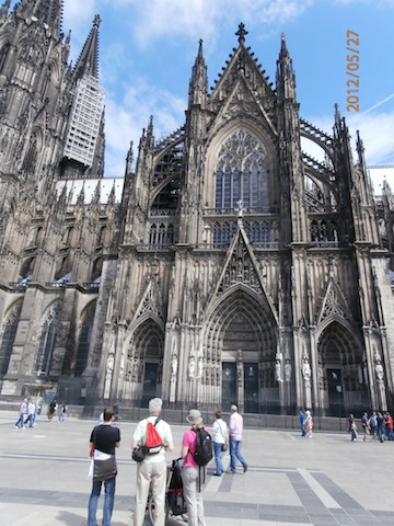 Across a nearly empty plaza, the ornate exterior of the cathedral
            rises toward a blue sky. The base of the bell towers can be seen
            on the left of the photo.