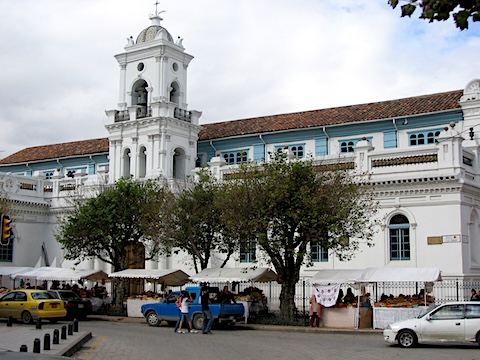 A bell tower is in the middle of the front of the
         building and vendors line the street.