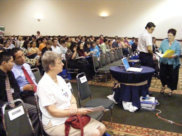 People gathering for the opening ceremony of the 
                  conference. Gail is sitting in a reserved seat in
                  the front row, and the first speaker
                  is getting set up.