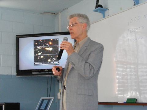 Al holds a cordless microphone to his mouth
                    with a panel showing blow ups from the Hubble
                    Deep Field in a corner of the room behind him.