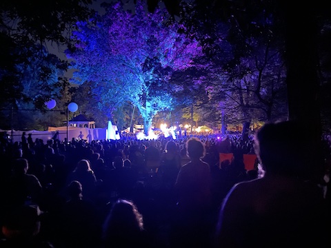 Many heads are visible in the dark in the direction of the performance area