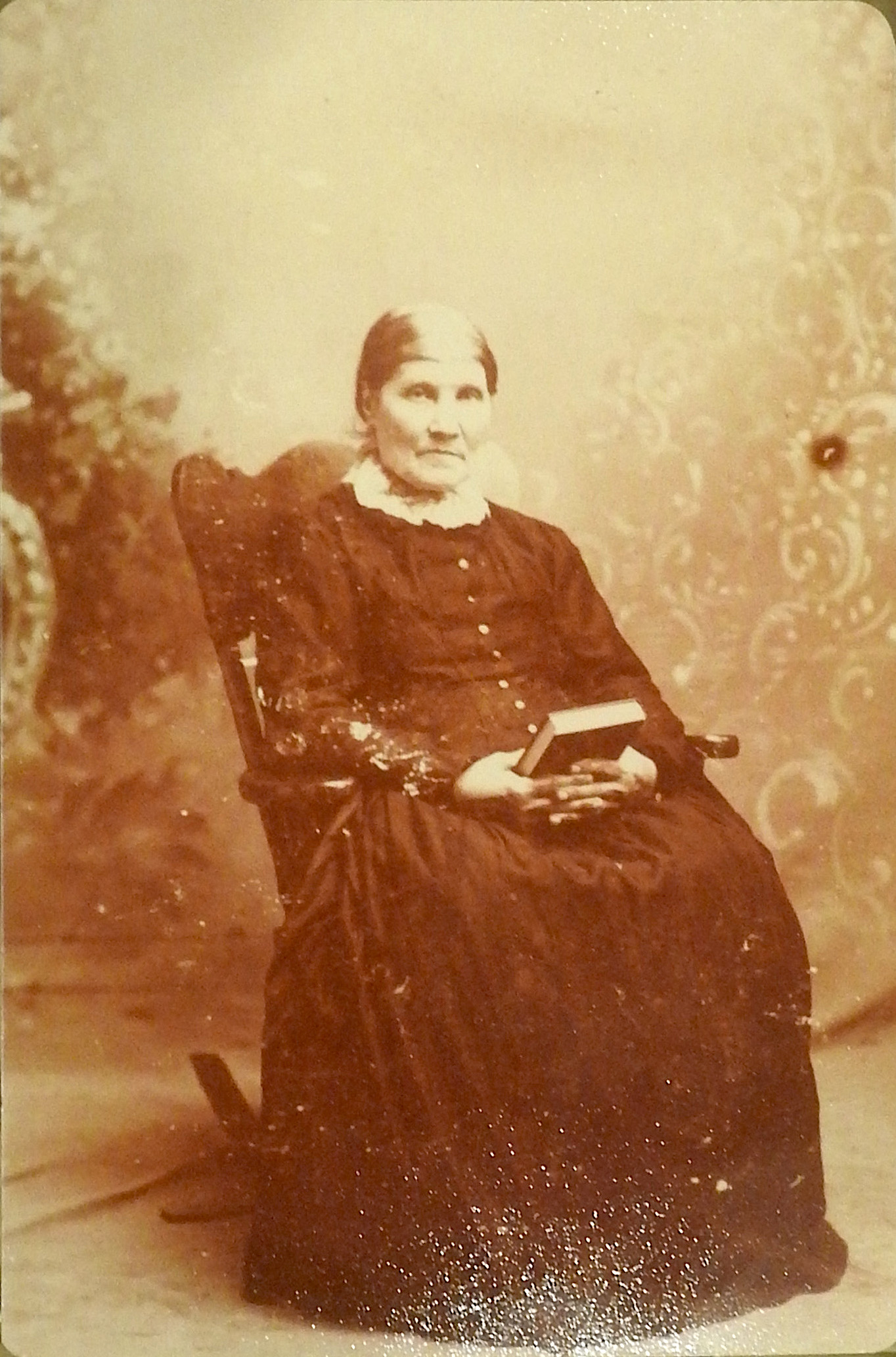 Eva Anderson is sitting in a chair and holding a book, possibly a Bible