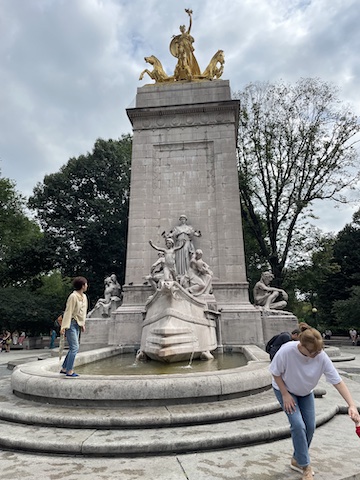 This is a tall stone monument with a fontain at the bottom and gilded 
                figures at the top