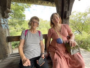 They are seated on a wooden bench with trees visible behing them