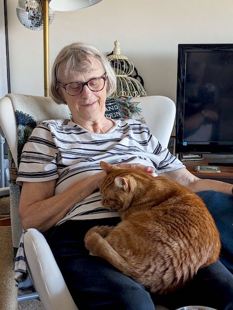 Oliver is curled up in the lap of Gail, who is in the rocking chair