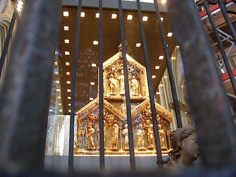 Seen through bars and glass (in which the stained glass windows
              behind the camera are reflected) is a pyramid formed by three
              gold pentagons, each featuring a Biblical scene.