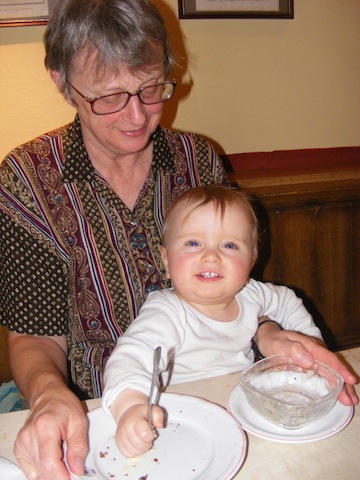 Gail is sitting at a restaurant table with a smiling
               Felix in her lap. Felix is looing right at the camera.