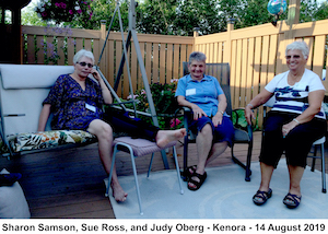 The three women are sitting in front of a fence and are looking at the 
               camera. 