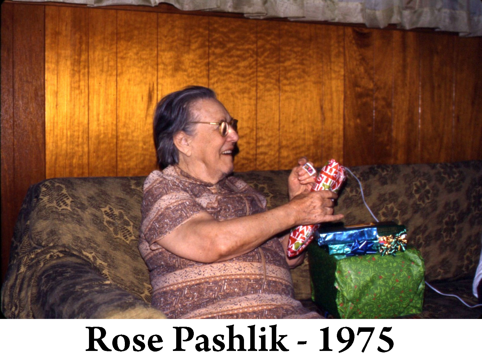 Rose is sitting on the sofa and smiling as she opens a gift-wrapped package. 