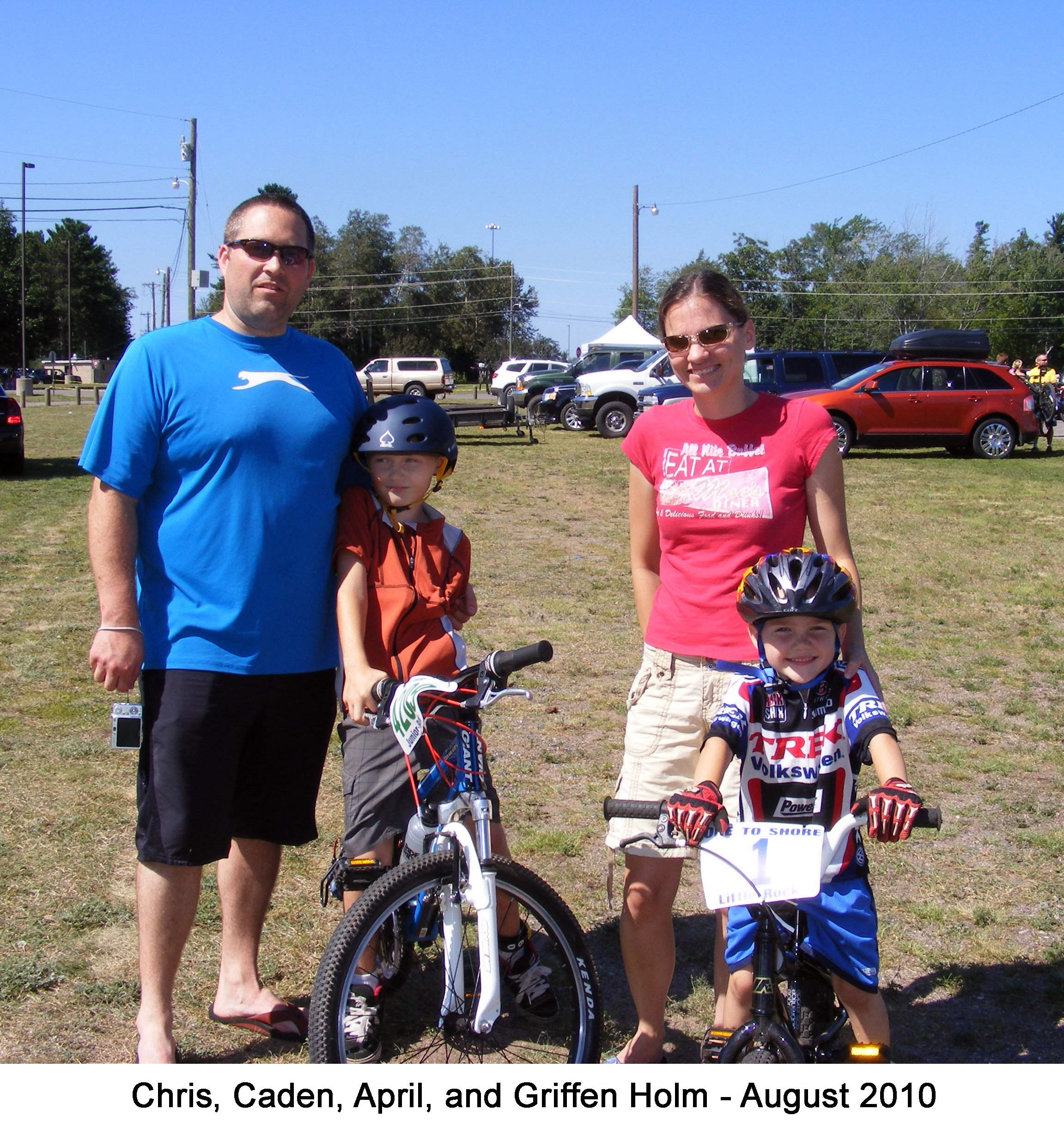 The family is standing in a field with the boys on their bikes. Cars are 
          parked behind them.