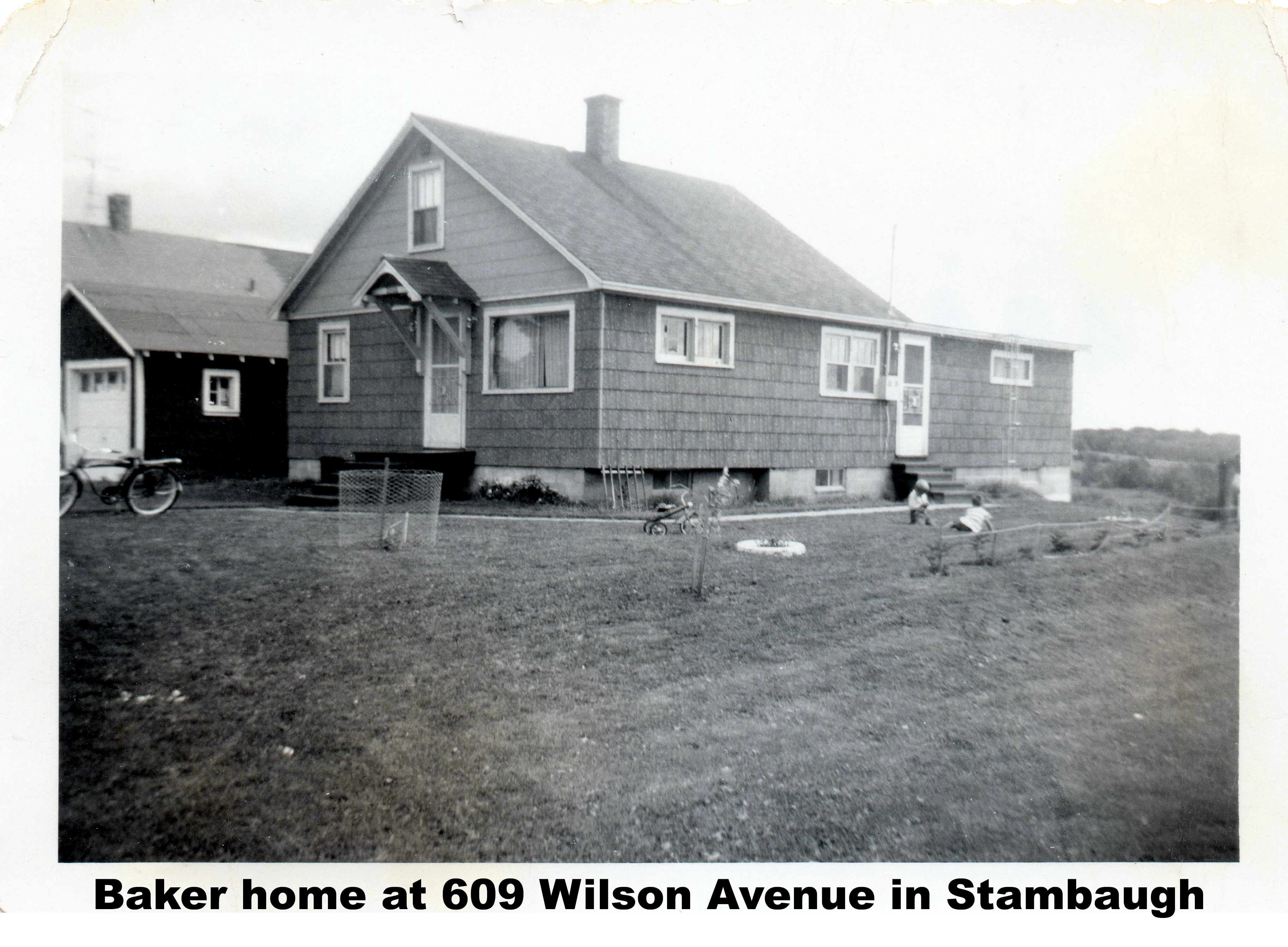 The house is seen from the southwest side. There's a door in the
front and one on the side and two children playing in the side yard.