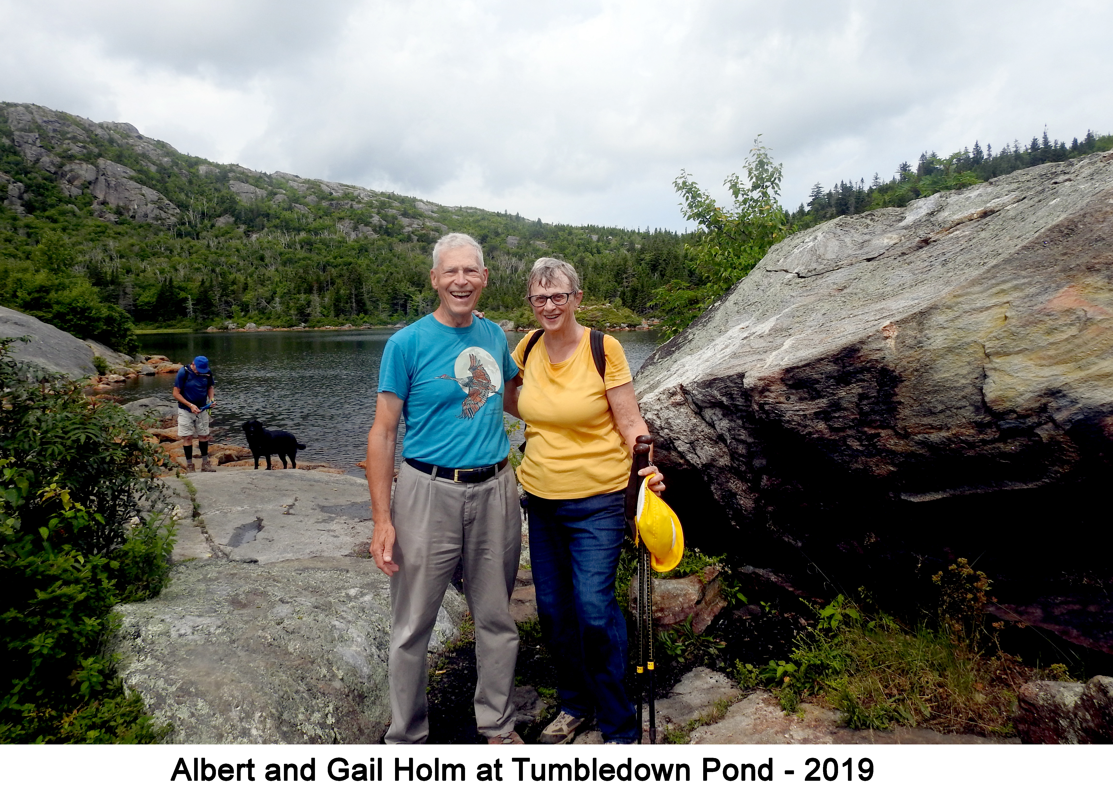 We are standing in front of the lake with a large boulder on the right
        side of the photo and Tumbledown Mountain on the left side