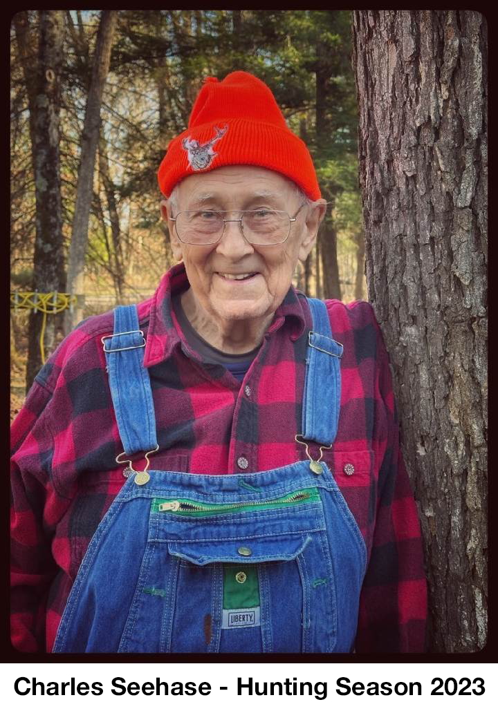Charles  is wearing a red hat and leaning against a tree
