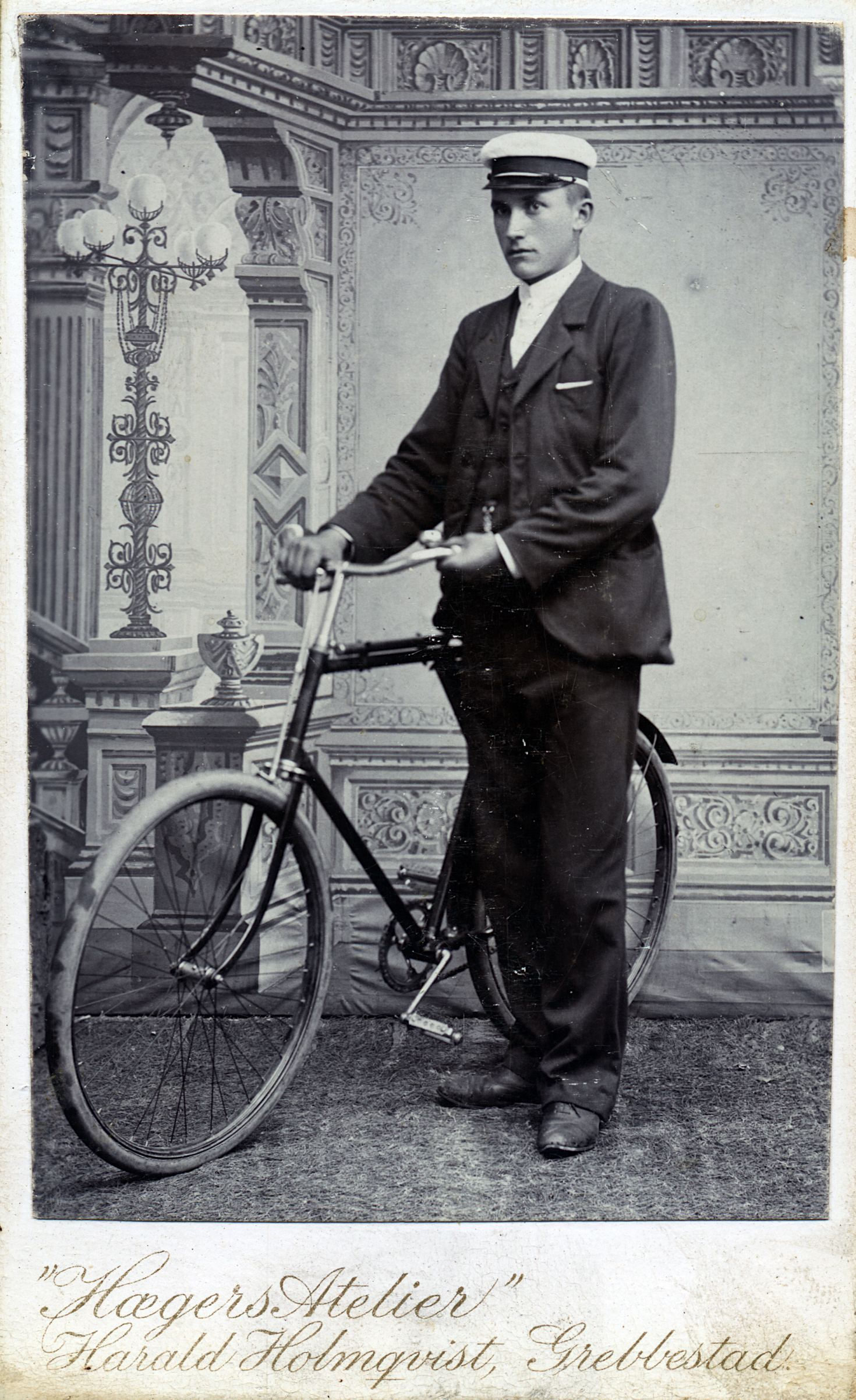 He is wearing a suit and a janty cap, and holding 
        pedal bicycle with pneumatic tires.