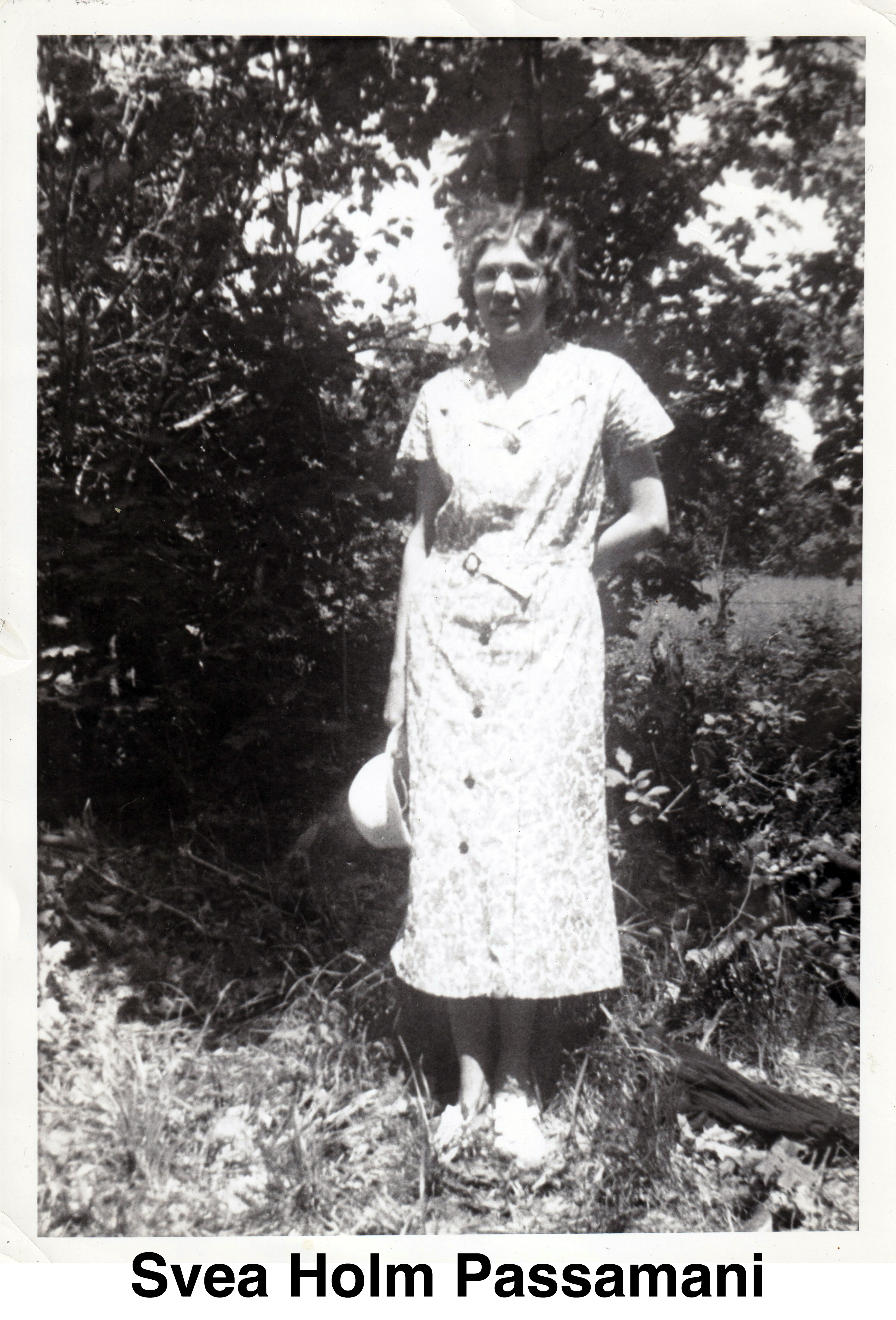 She is wearing a light dress and holding a hat in her right hand. 
         She’s standing in front of trees.