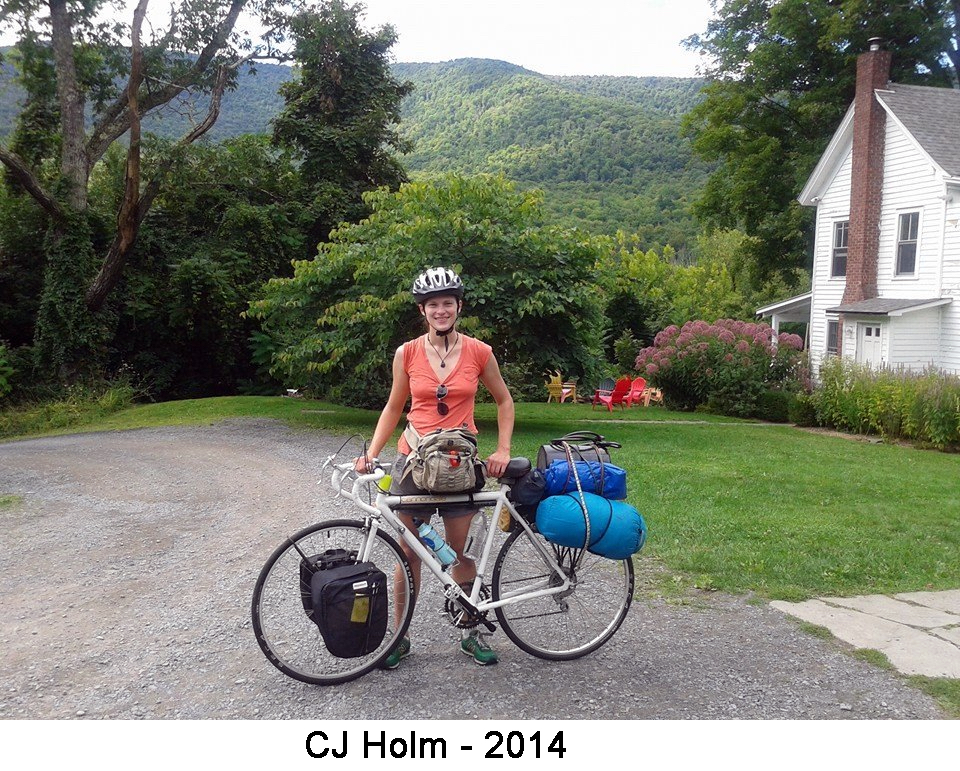Standing with her bike, she's wearing a helmet.  sleeping bag and tent 
     are attached by the back wheel, and panniers are attached at the front wheel.