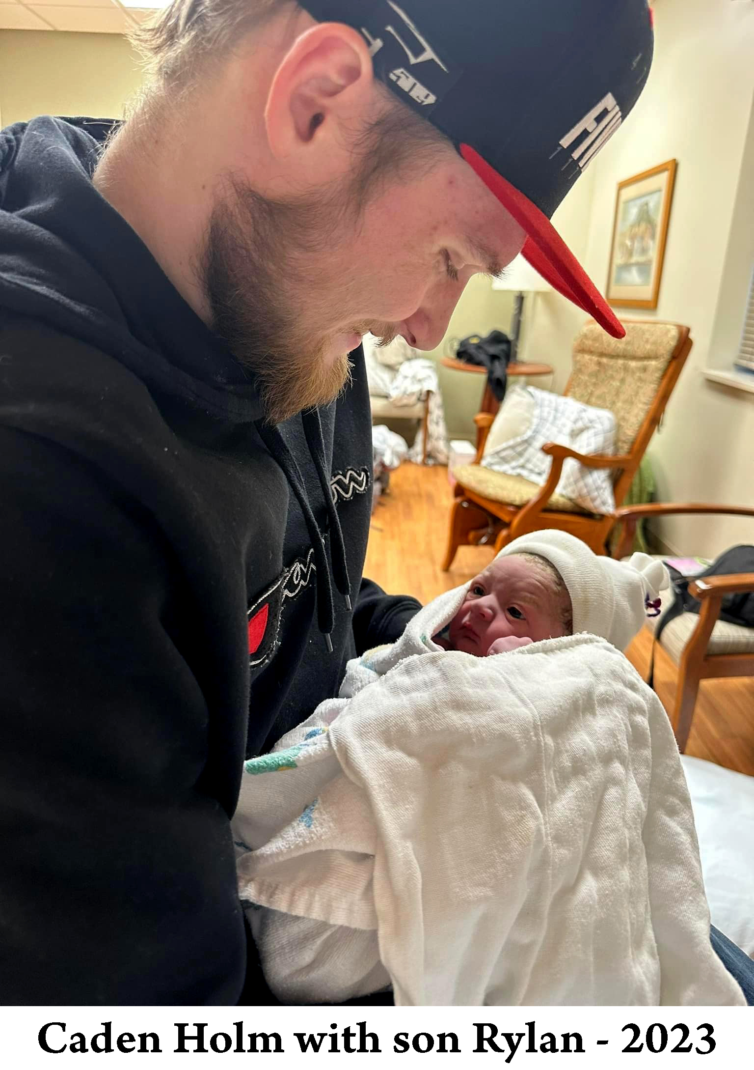 Caden Holm is holding his son Rylan and gazing down on him 