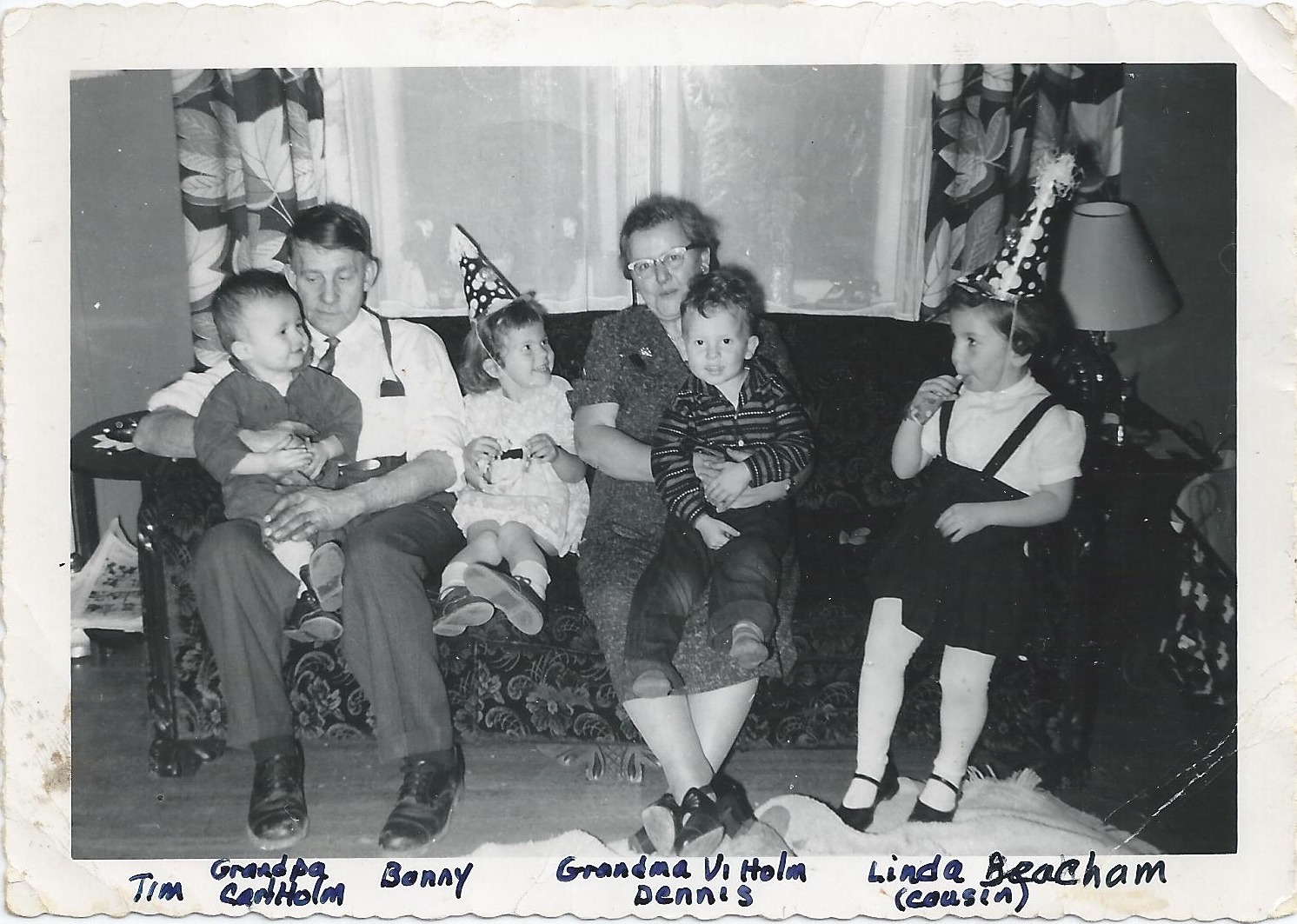 They are all seated on a long sofa. Carl is holding Tim and Violet is holding
          Dennis. The girls are wearing conical party hats.