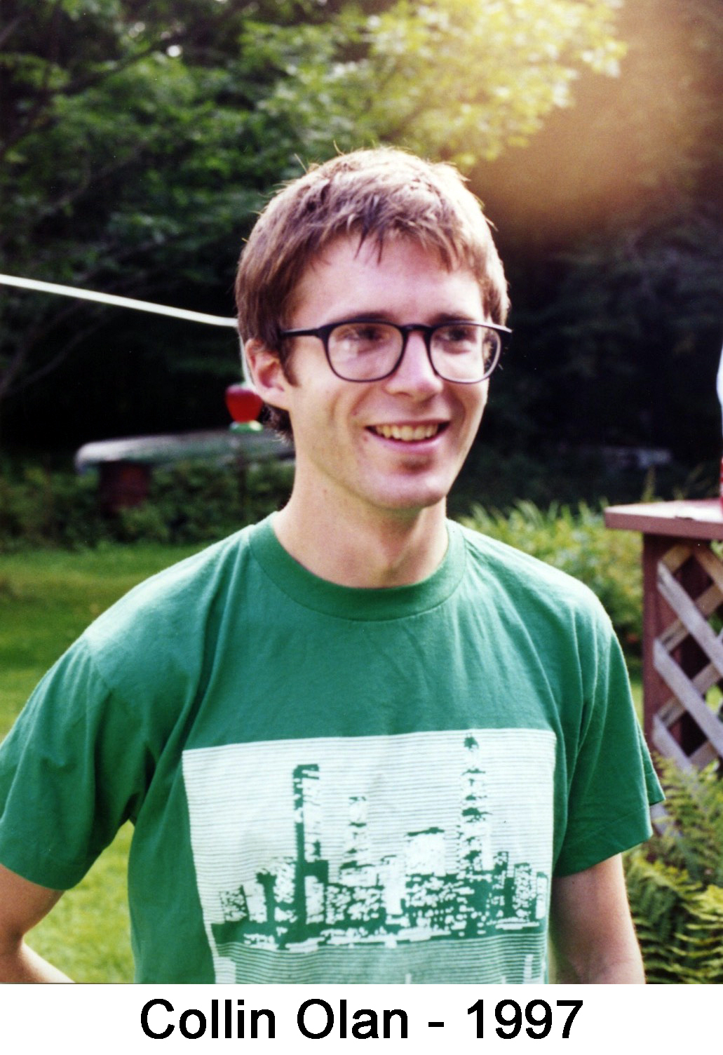 He is smiling and wearing glasses and a green T-shirt.