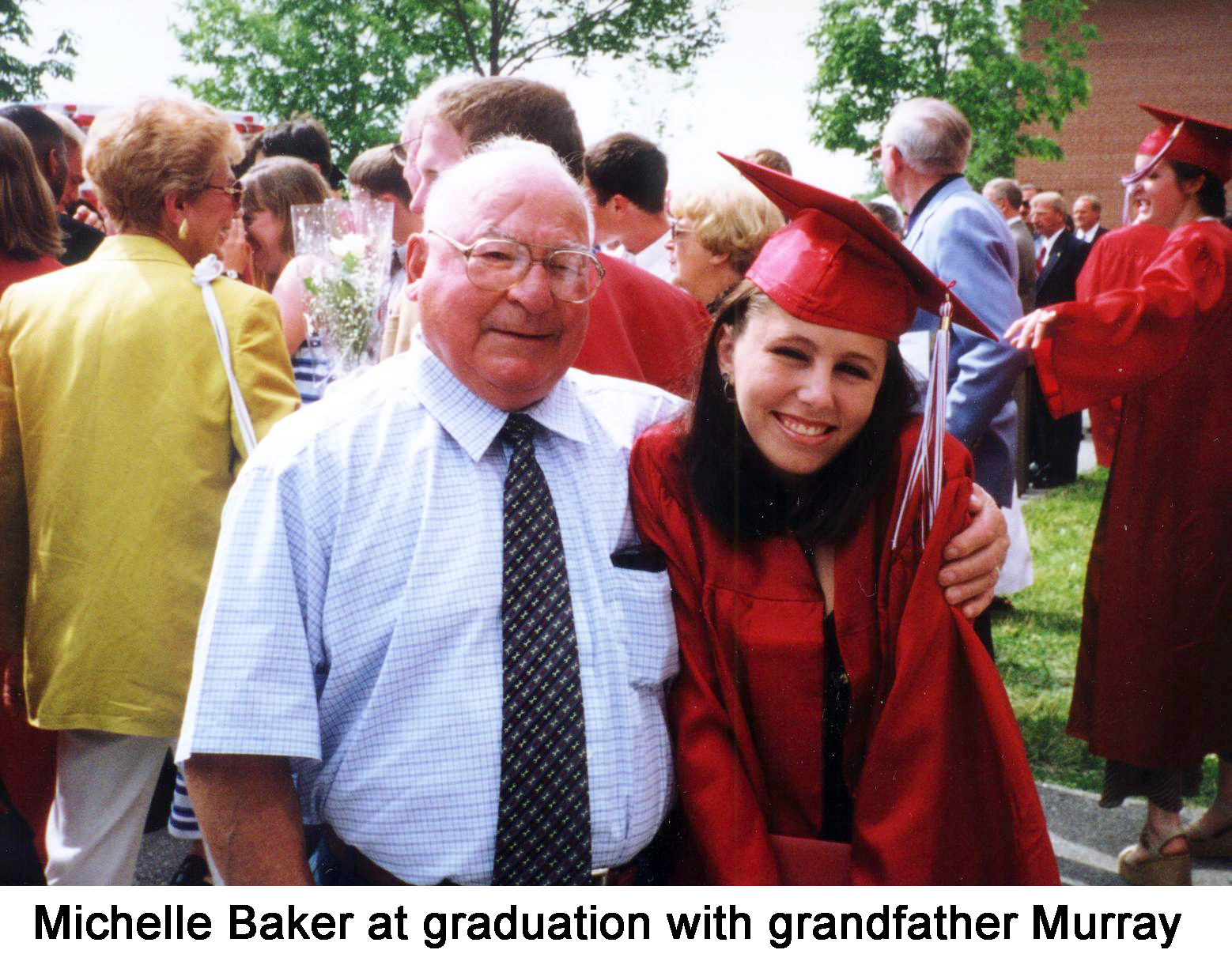 The granduates are wearing red robes. Murray has his arm around Michelle.