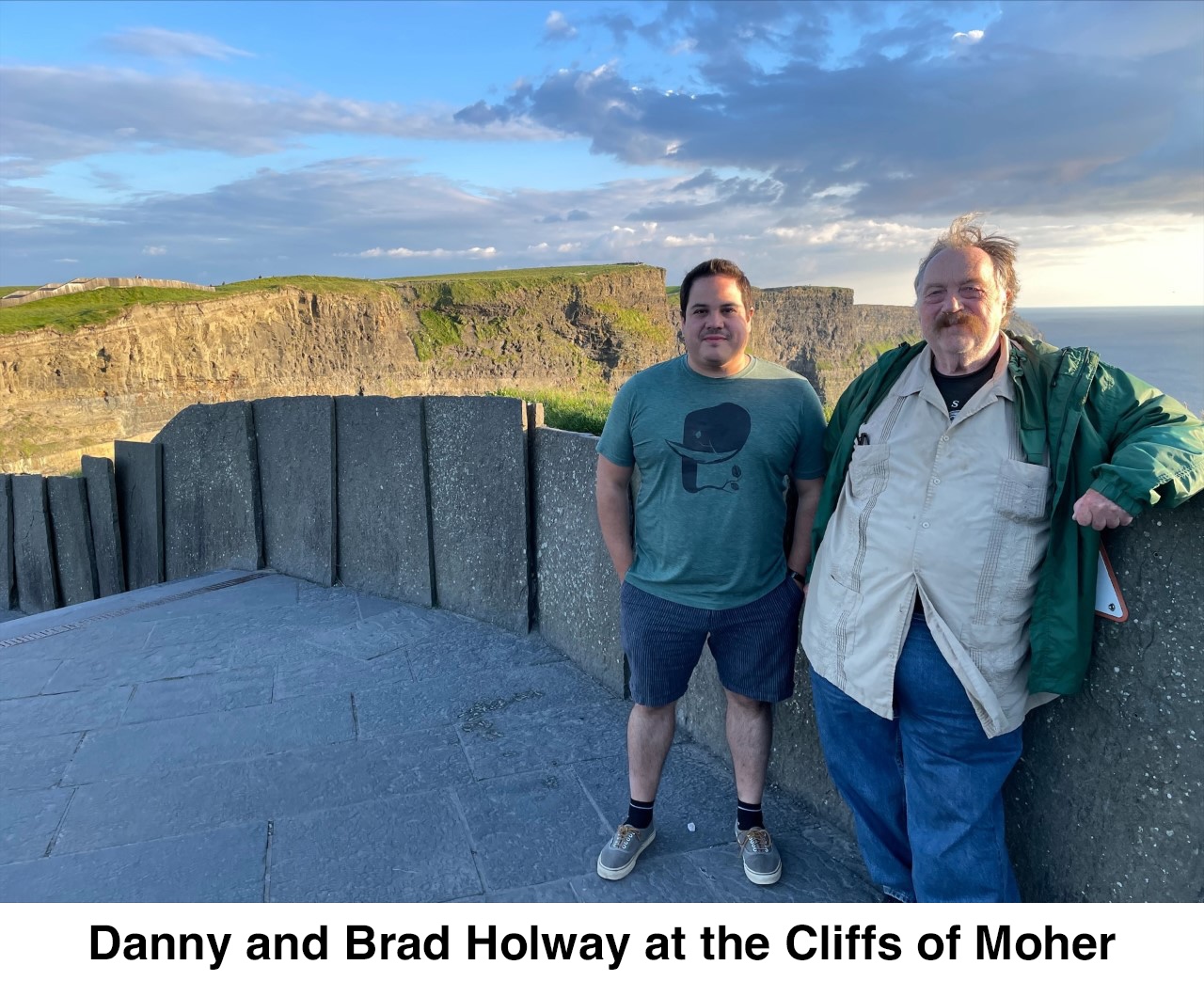 Danny and Brad are standing next to a wall. The cliffs are visible in the 
       distance. The sea is visible in the distance on the right.