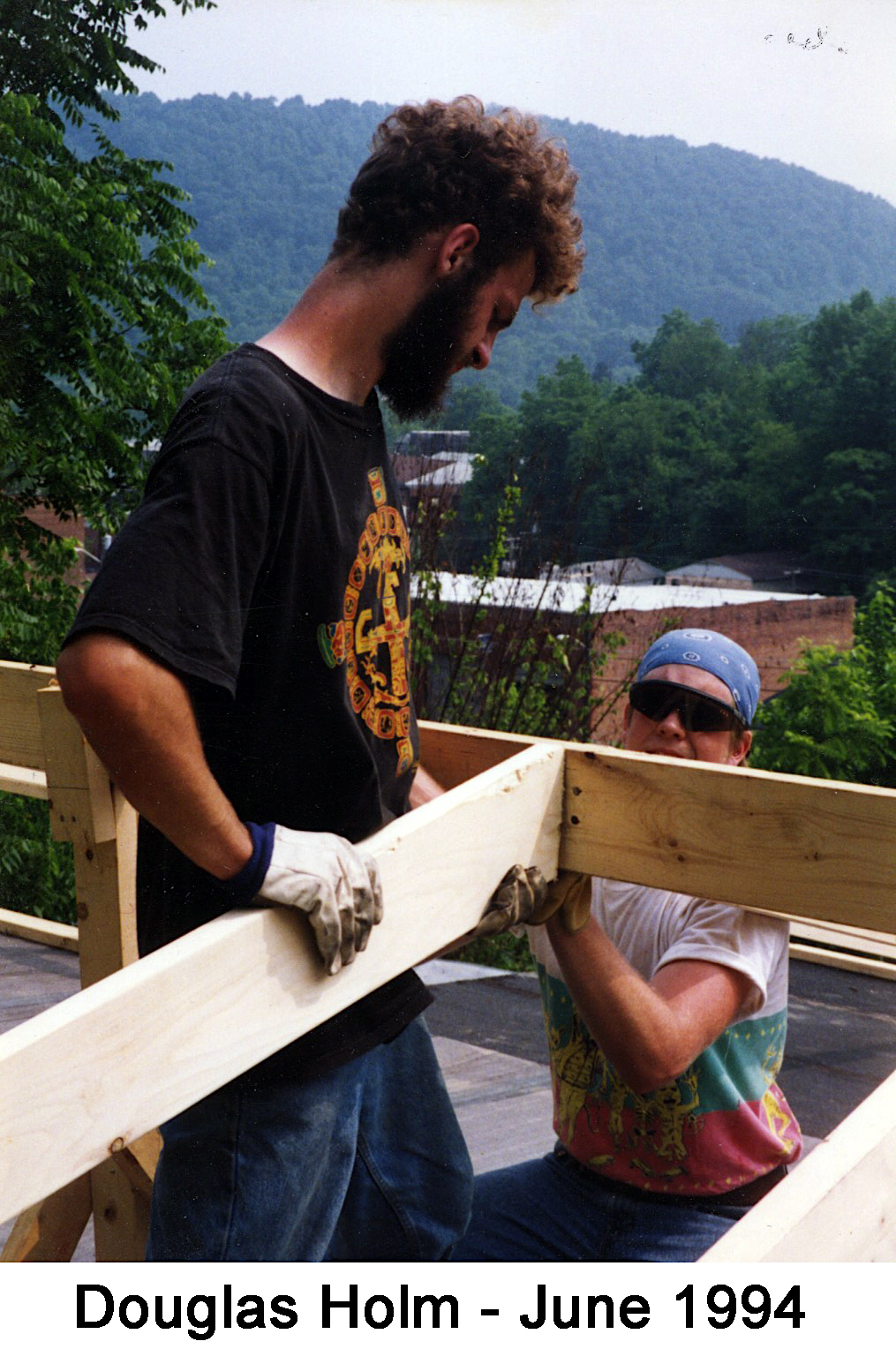 Doug’s back is to the camera. He is holding a rafter in place while another
        member of the crew fastens it. 