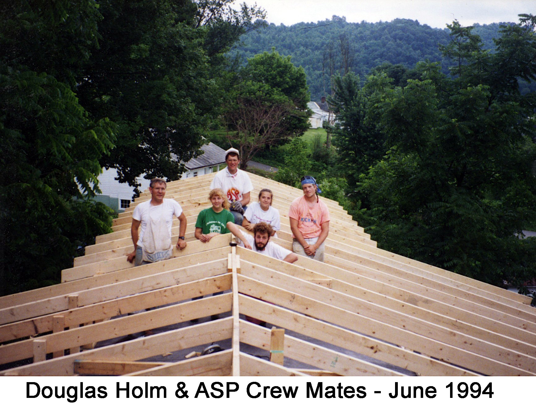 The six member crew is on top the mobile home among the rafters 
          they have assembled for the roof.