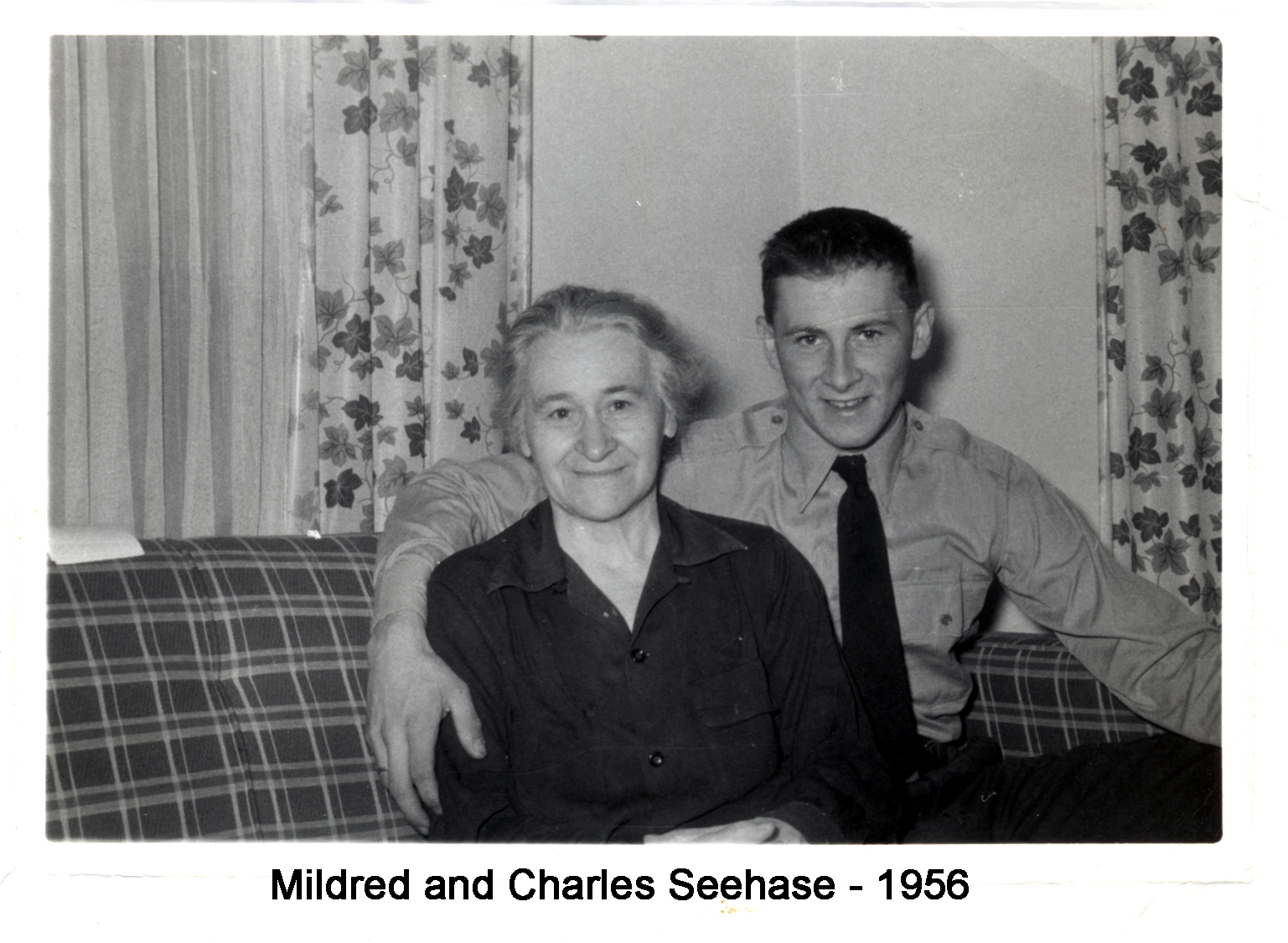 They are sitting together on a sofa, both smiling at the camera