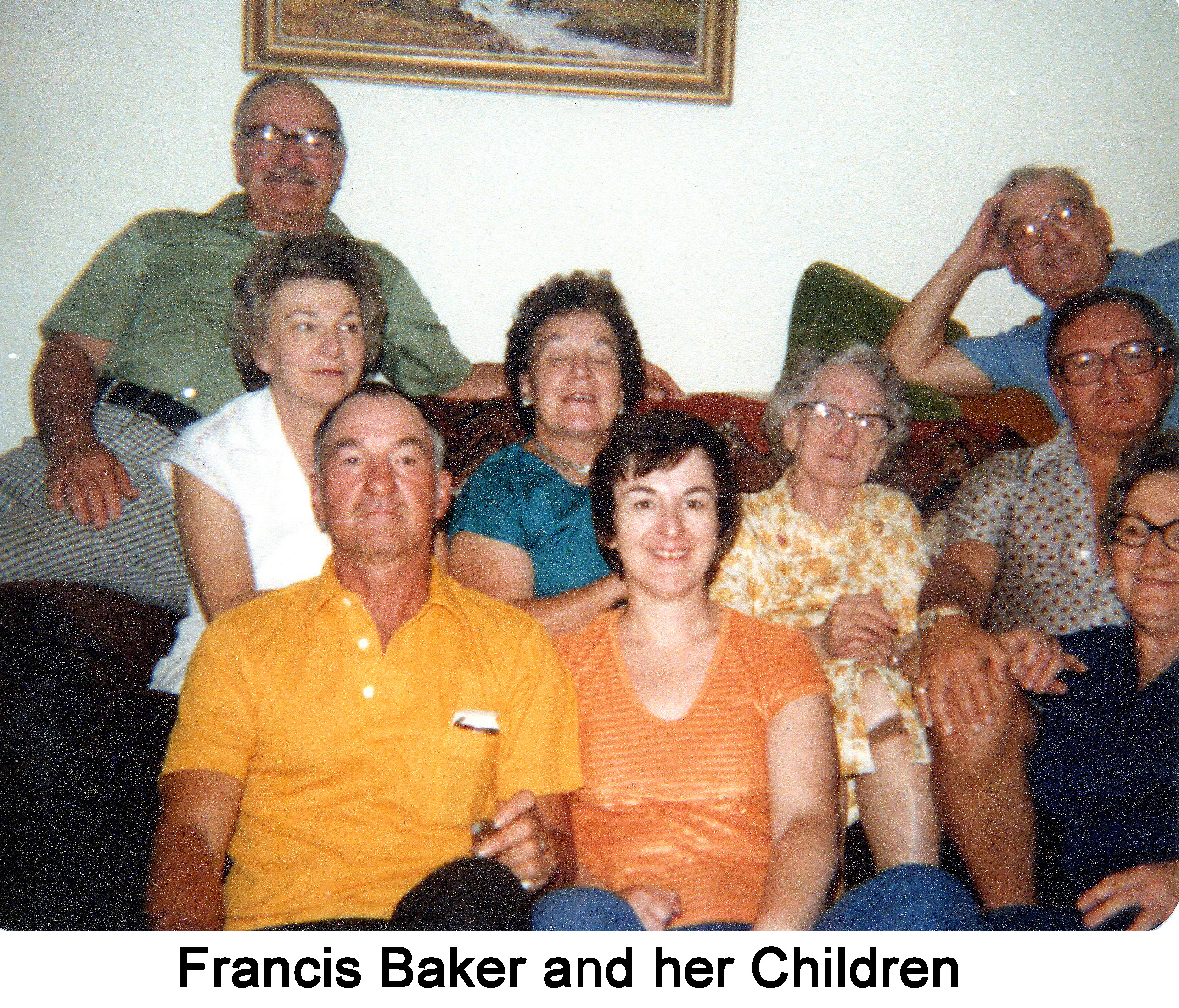 She is seated on a sofa with the adult children beside, above, and 
     in front of her.