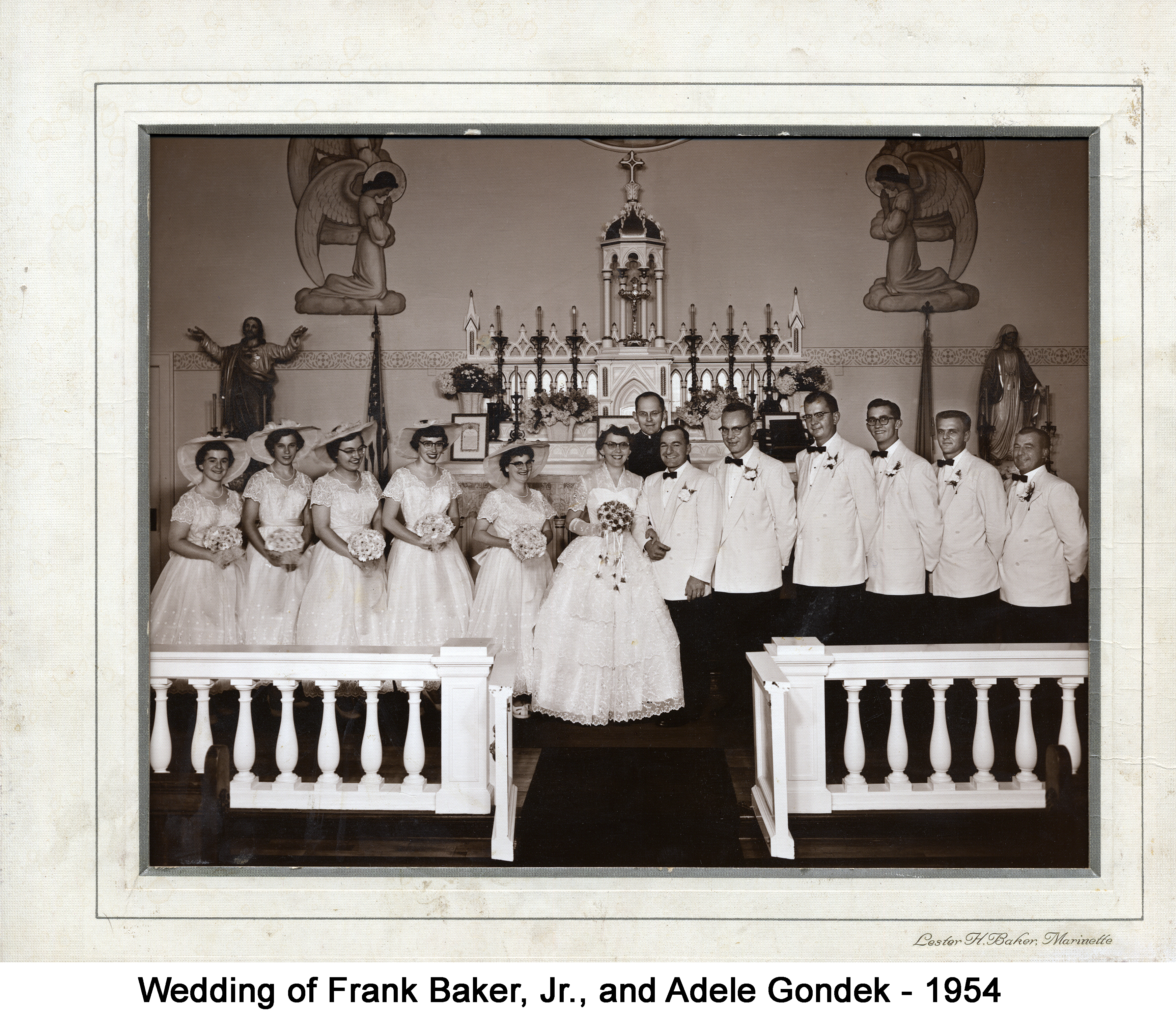 A large wedding party is standing in front of the altar with the priest standing
          behind them. The women all are in white dresses with large brimmed hats and the
          men are in white jackets.