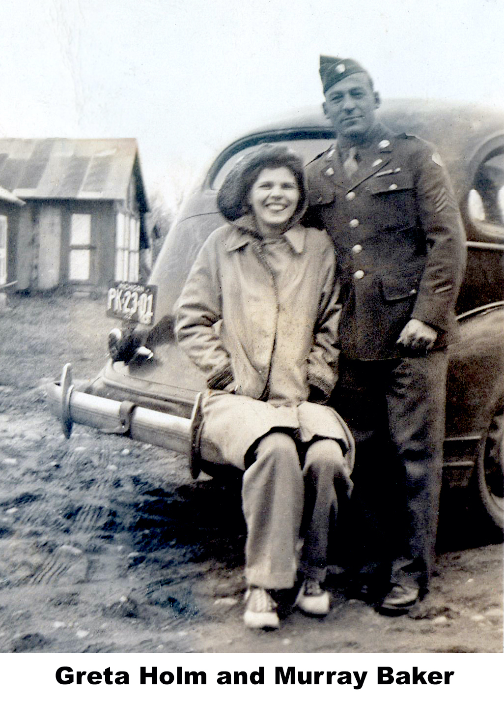 Greta Holm and Murray Baker by a car at Victor Holm’s home. 
     Greta, in a warm coat, is siting on the back bumper and Murray, in his uniform,
     is standing beside her.