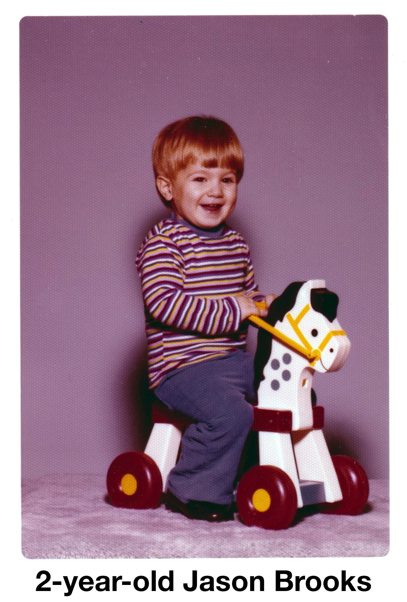 Jason is riding a toy horse on wheels in a studio photo