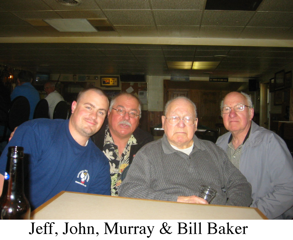 Jeff, John, Murray, and Bill Baker are sitting behind a small table, 
        a dark room, probably Jacobetti's fellowship hall.