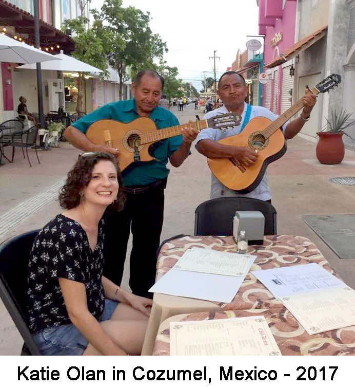 She is sitting at an outdoor table in the middle of the street with two 
          guitarists playing behind the table