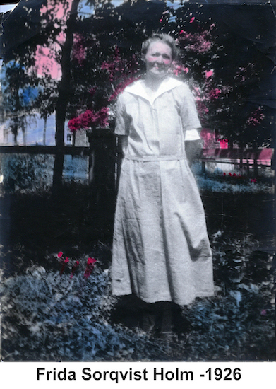 Frida Holm wearing a white dress and standing in front of flowering shrubs