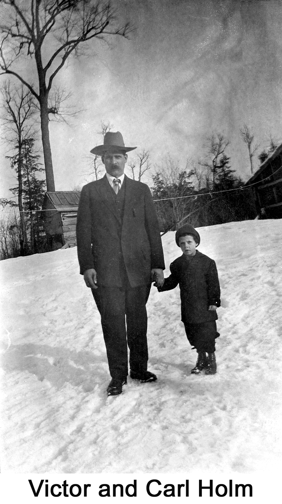 Victor and Carl are standing on snow with wooden buildings behind them.
        Victor is holding Carl’s hand. 