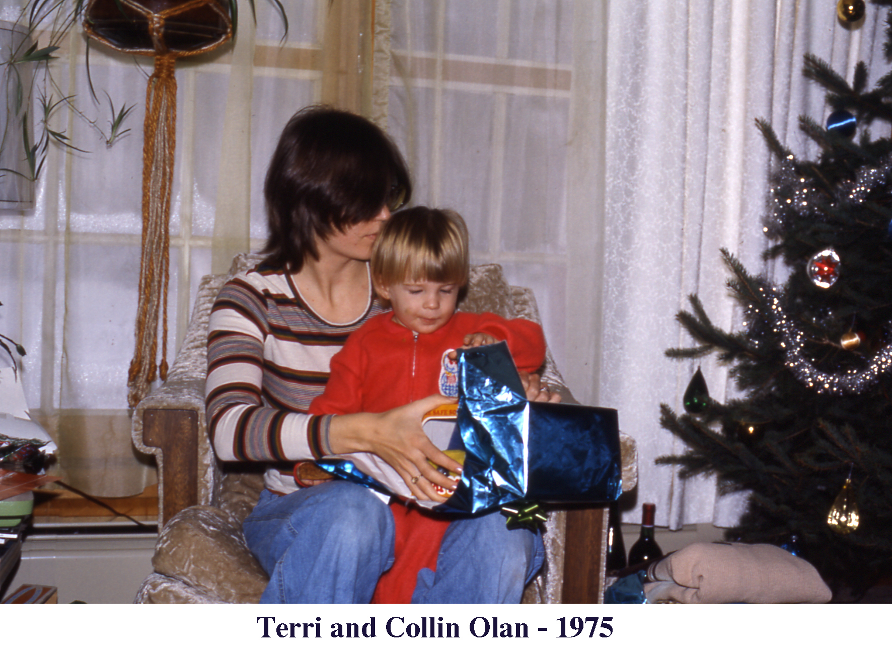 Terri and Collin Olan sitting in a chair and opening a blue-wrapped gift 
       at Christmas 1975