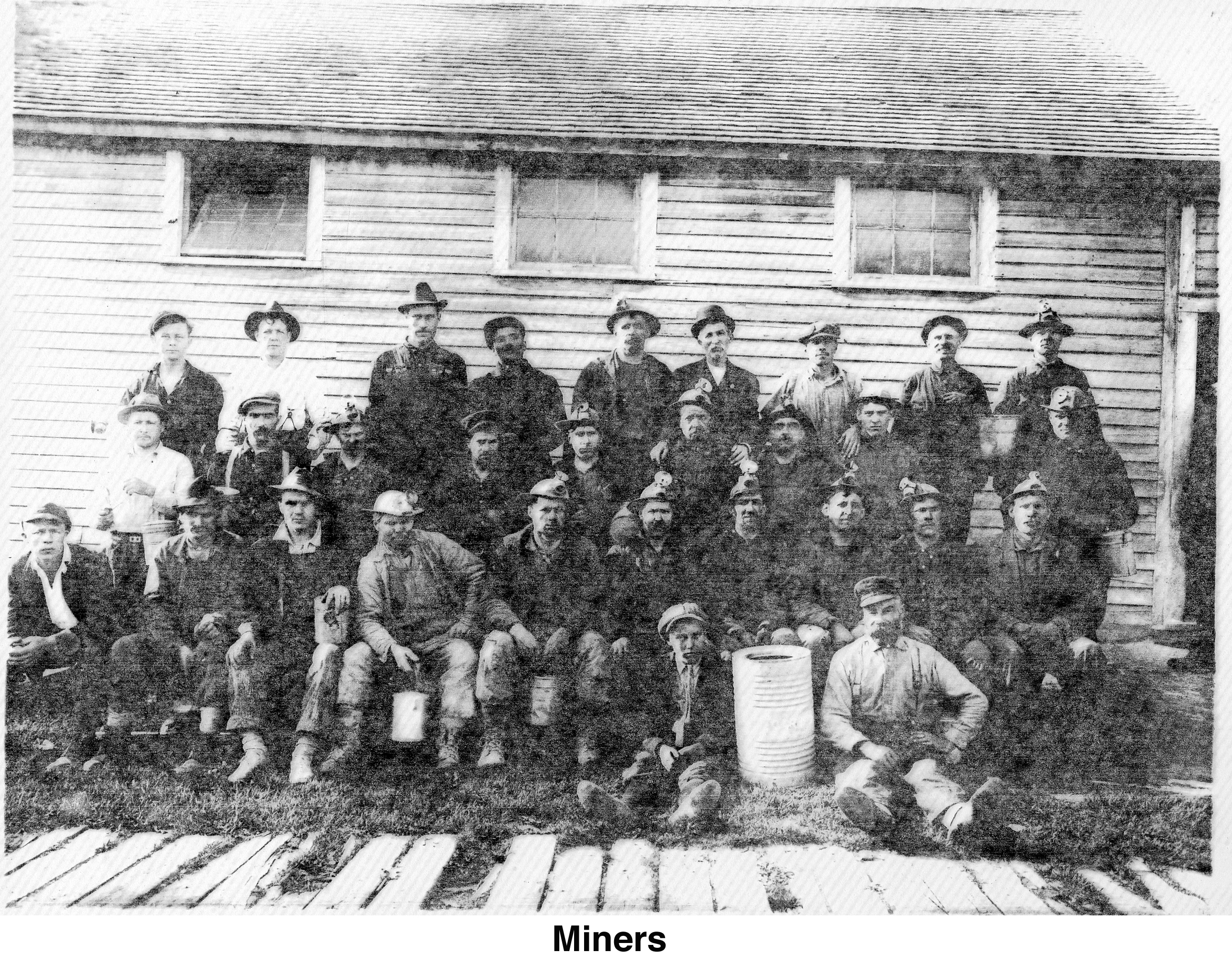 Men in mining gear in front of a building with wood siding.