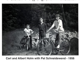 Carl is leaning against his bike, Pat is astride hers. 
                    Albert is standing. A pile of bricks are behind them.