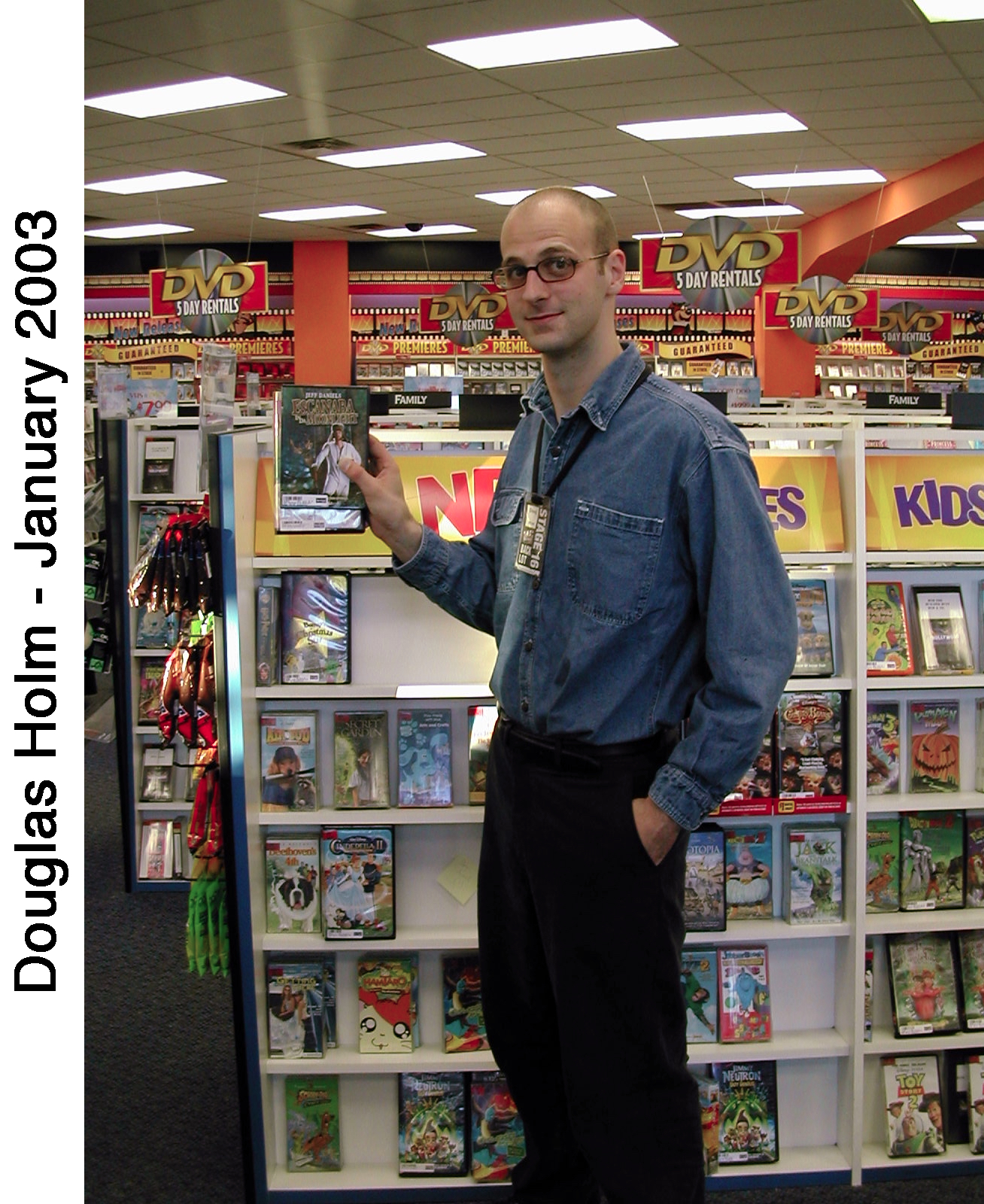 Doug Holm is standing next to shelves of videos and holding a box