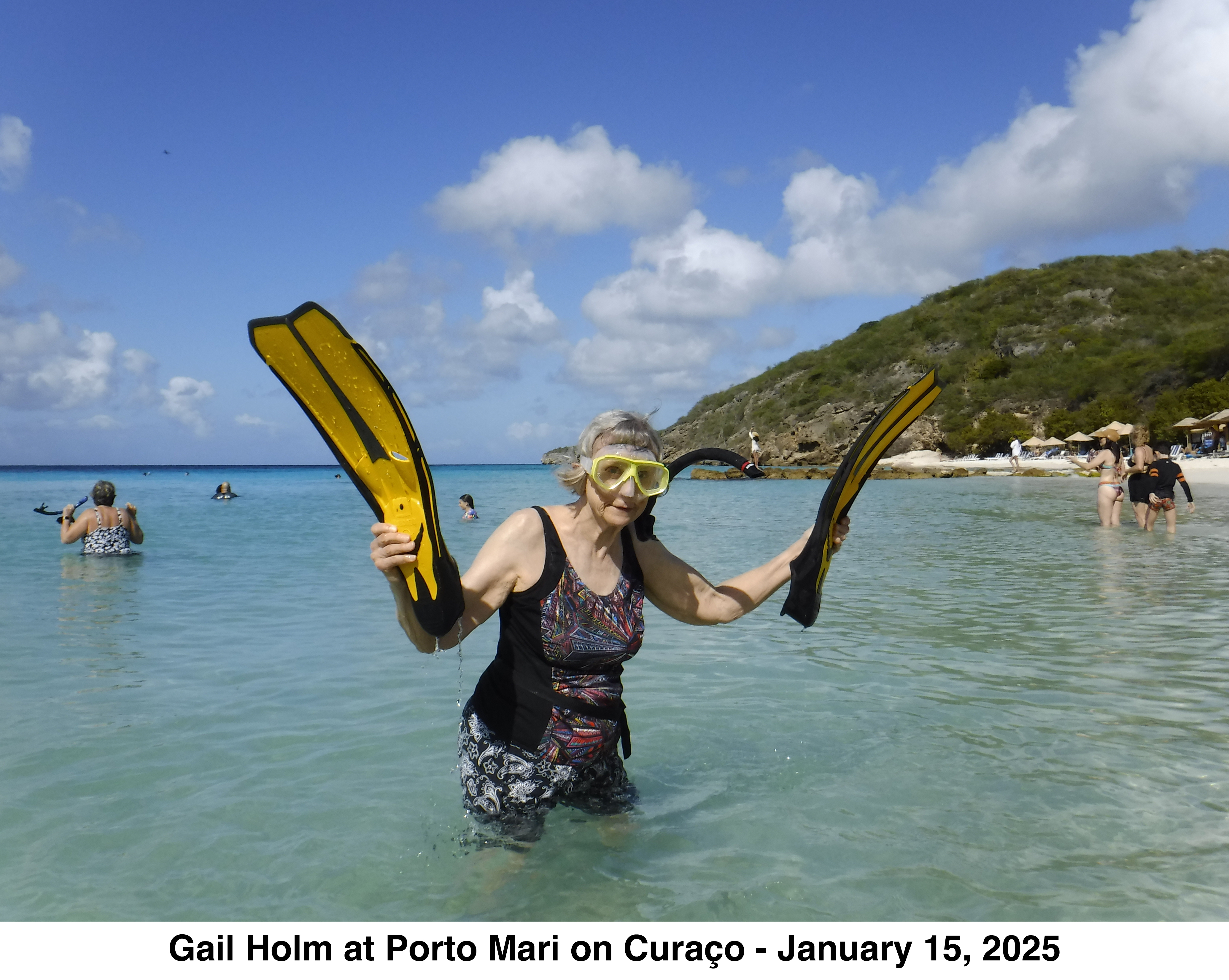 Gail Holm is standing hip deep in the water, wearing her mask and snorkle, and
               holding her swim fins. 