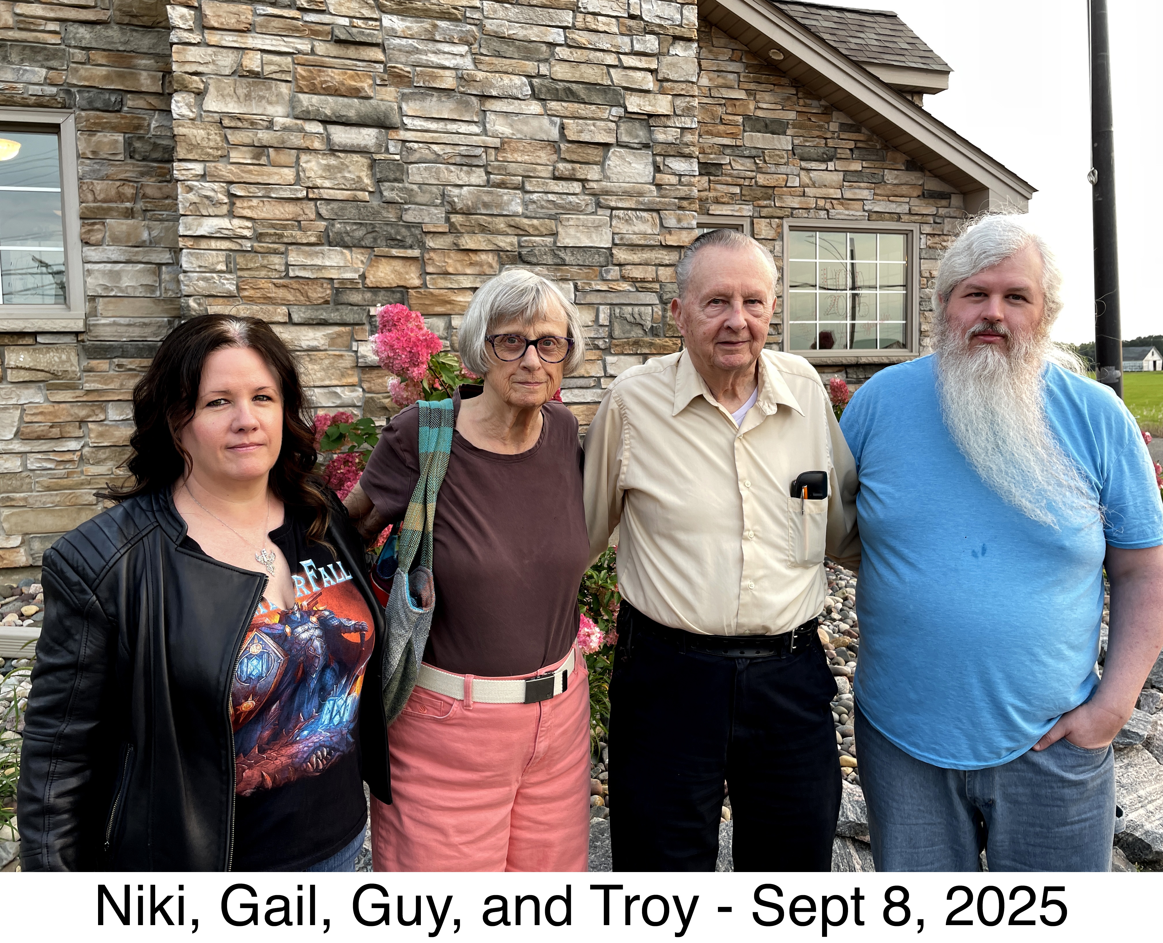 Gail, Guy, and his family standing in front the stone wall of the restaurant