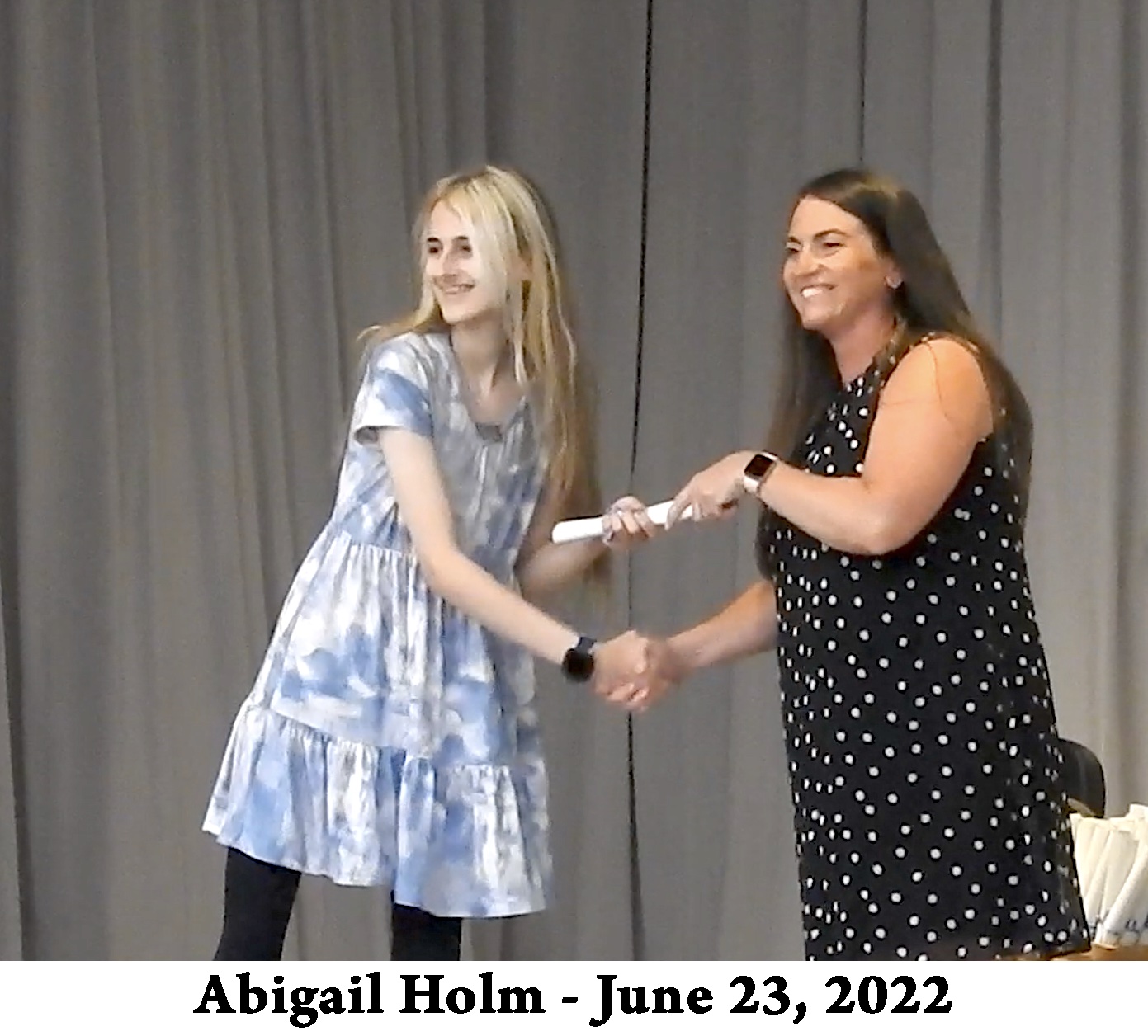 Abby holds her scroll and the hand of the Principal on stage