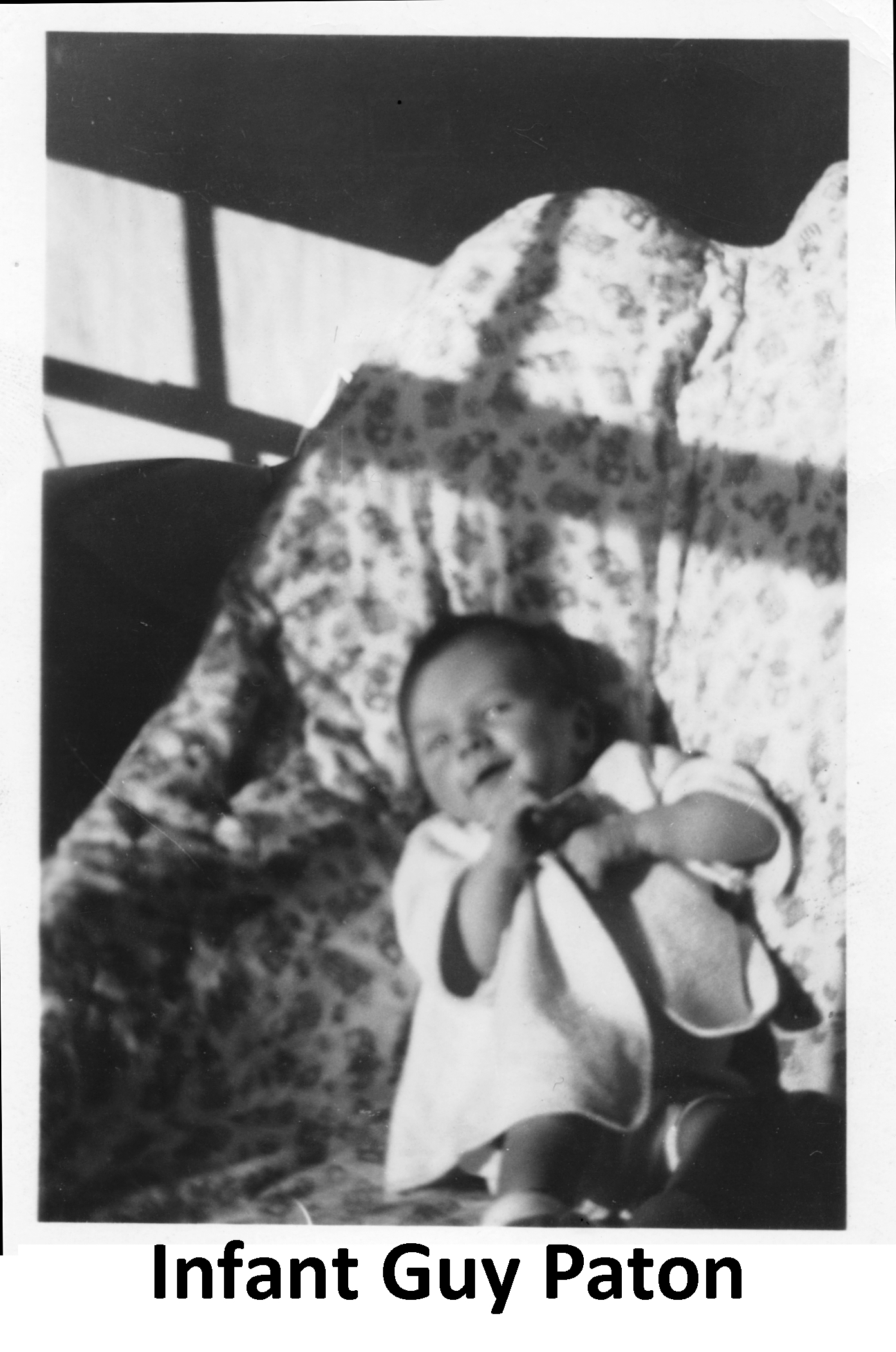 The smiling infant Guy Paton is lying on a leopard-spotted blanket