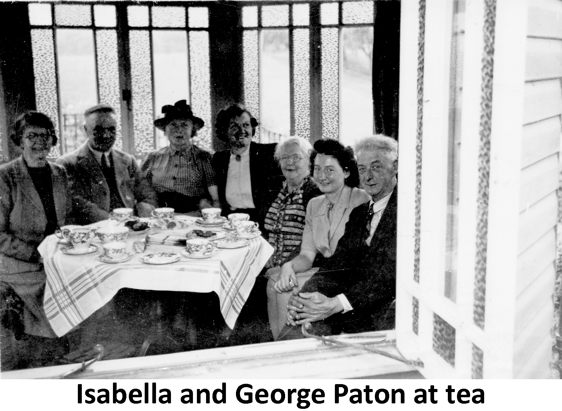 George and Bella Paton at tea  seen through the window of a house