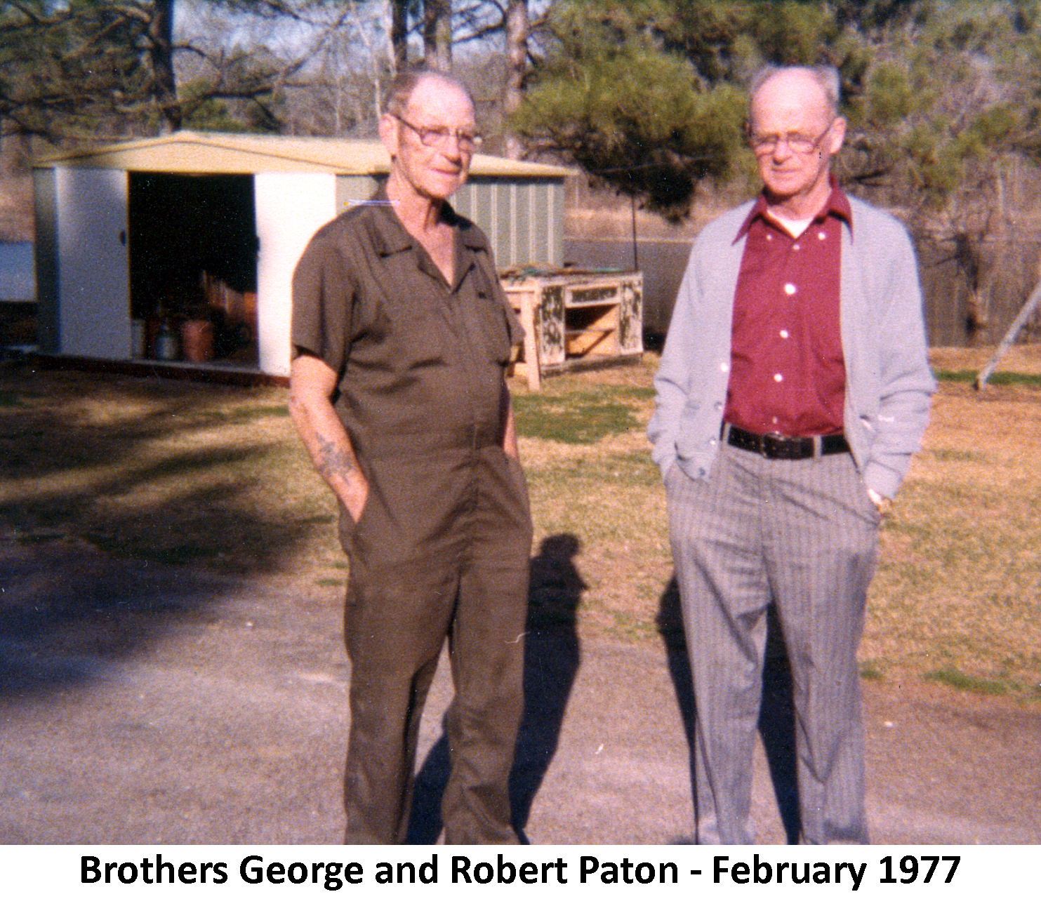 George and Robert Paton standing in a yard with a large utility shed and pine trees