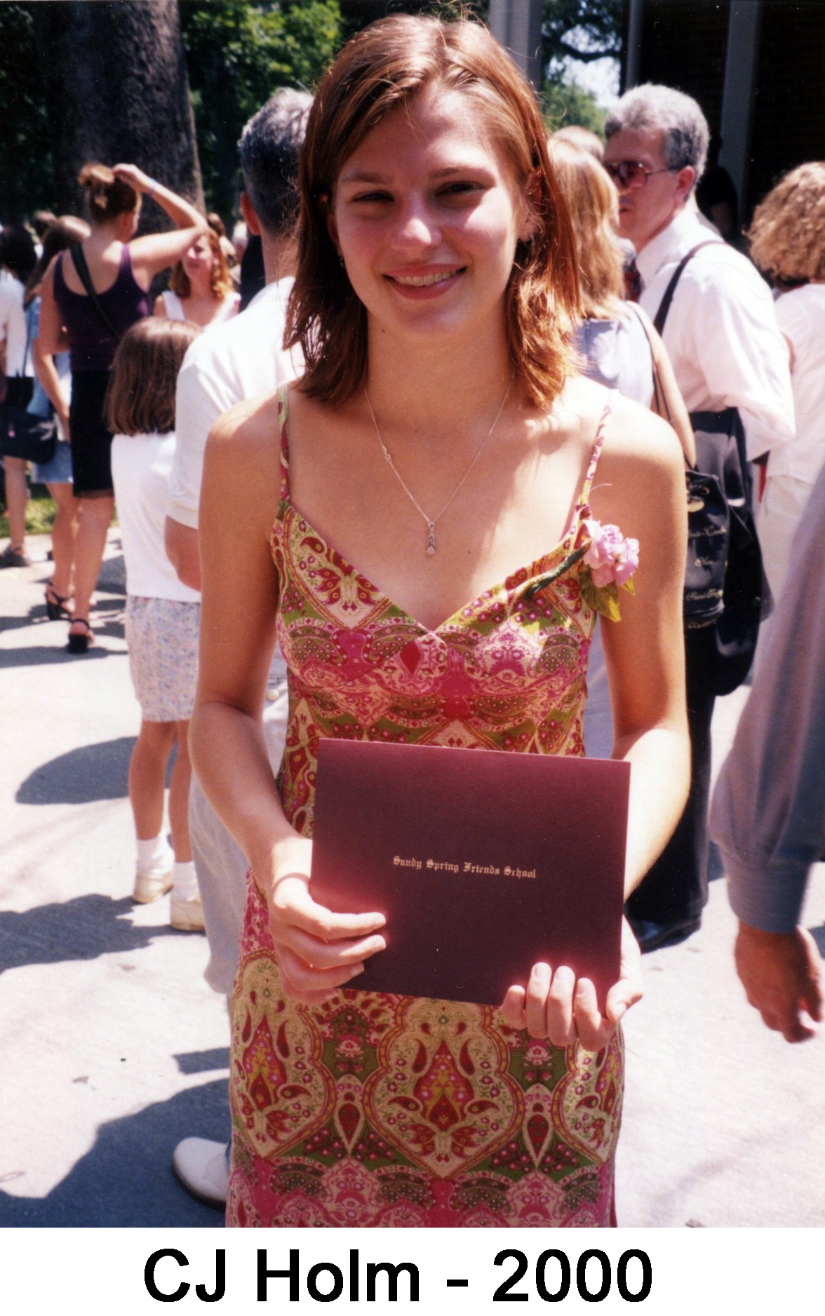 She is wering a colorful dress and holding the maroon diploma case
