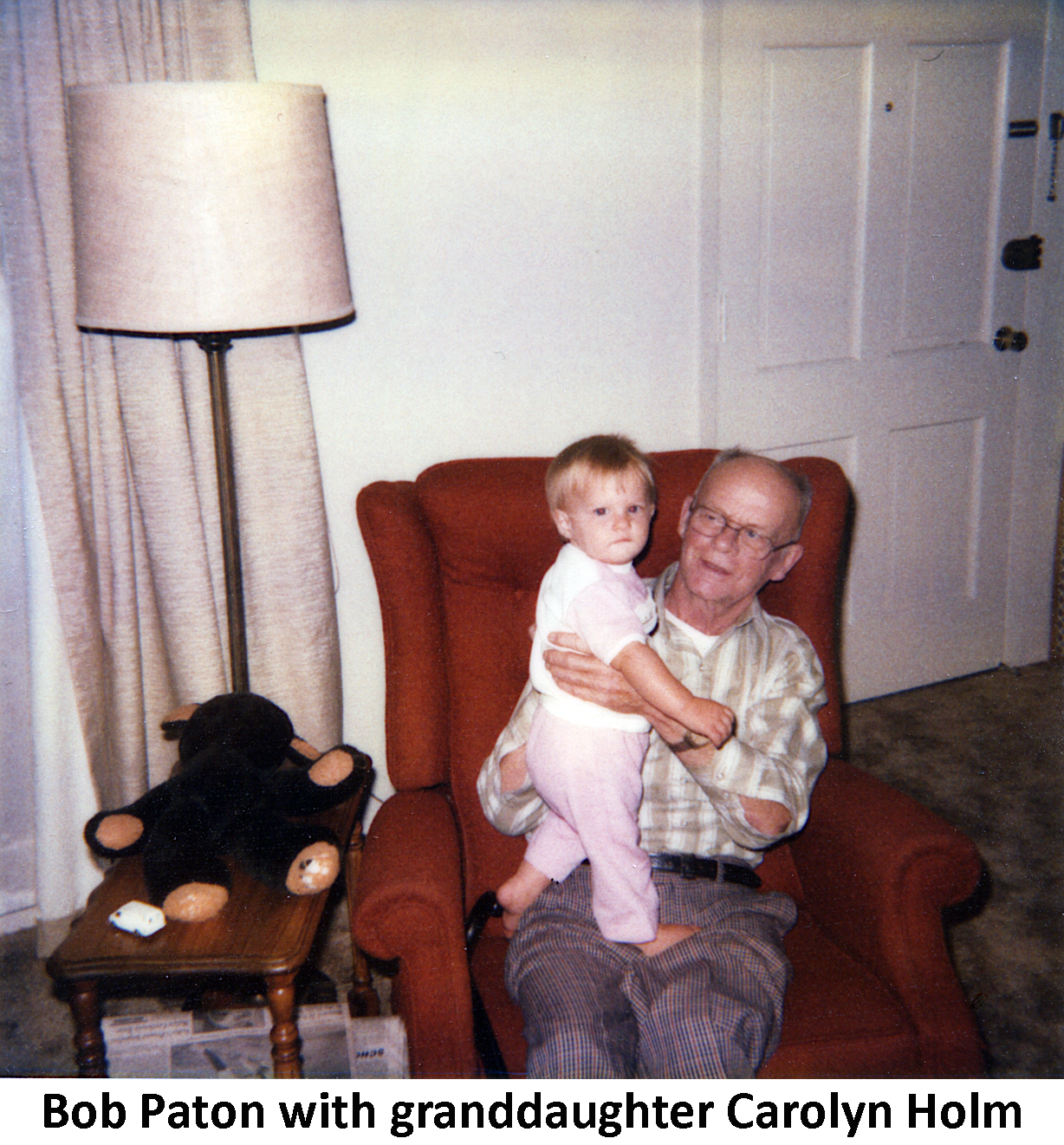 Bob Paton seated in an orange recliner with Carolyn Holm 
             standing on his lap.