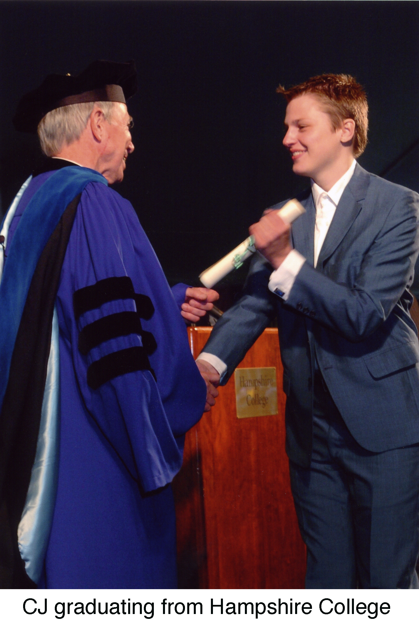 CJ Holm, in a suit, graduating at Hampshire College, receiving a scroll 
          from the blue-robed college president